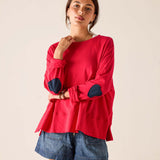 Woman wearing a red long-sleeve top with navy elbow patches against a beige background