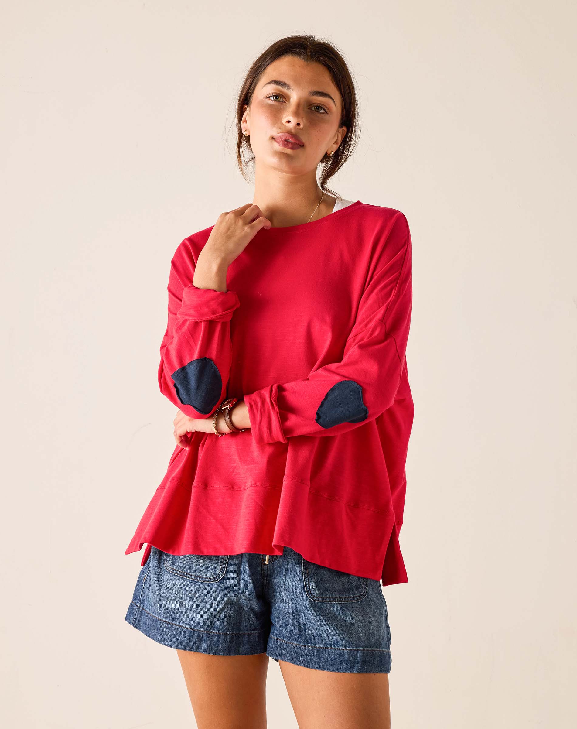Woman wearing a red long-sleeve top with navy elbow patches against a beige background