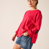 Woman wearing a red sweatshirt and denim shorts on a plain background