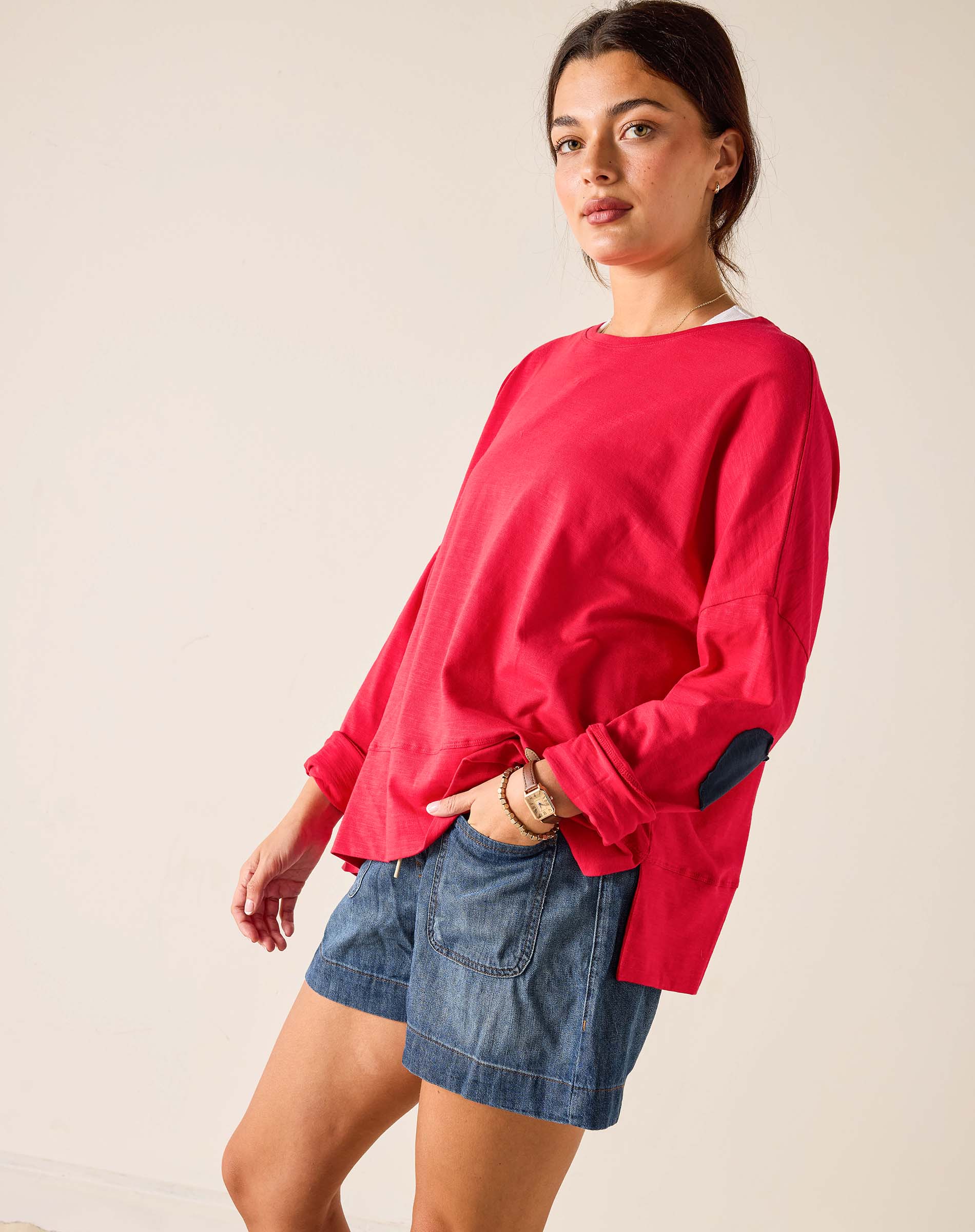 Woman wearing a red sweatshirt and denim shorts on a plain background