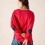 Person wearing a red long-sleeve shirt with navy elbow patches on a beige background