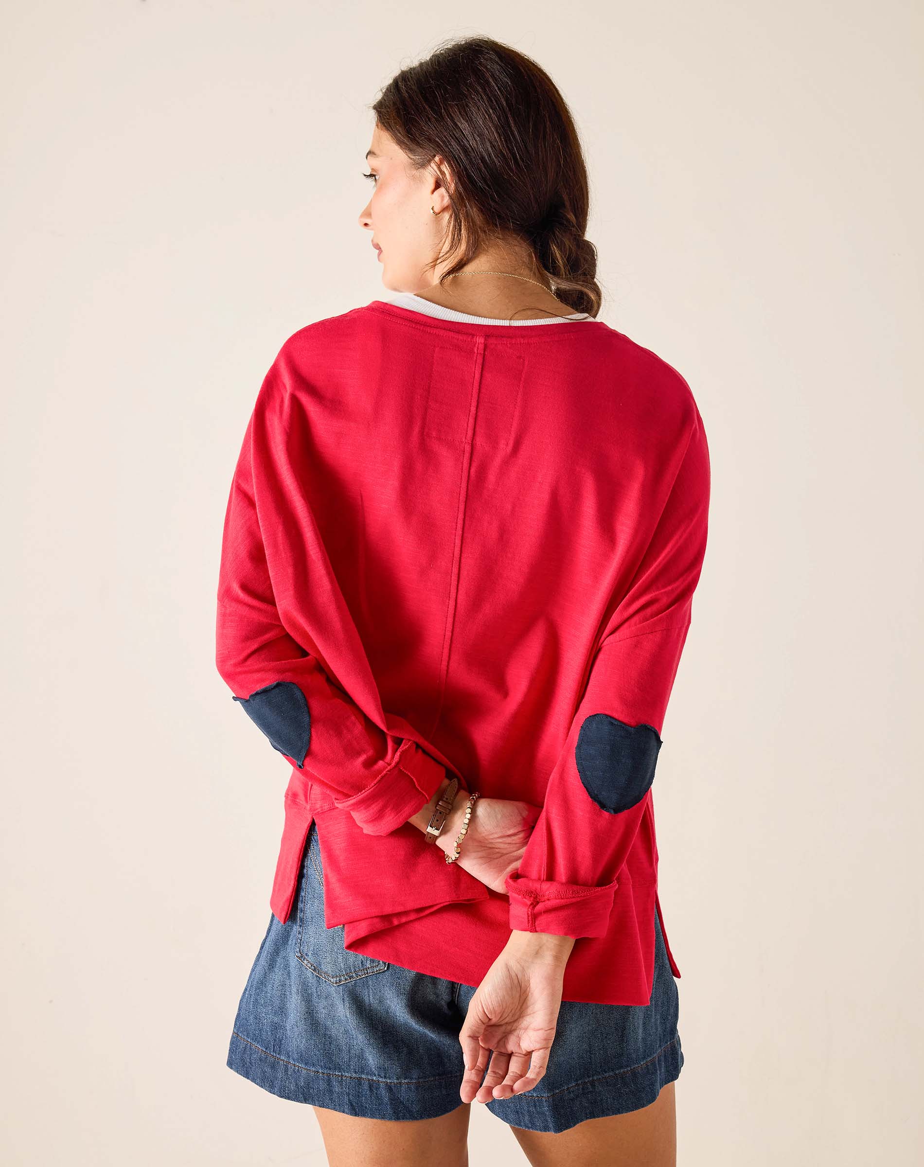 Person wearing a red long-sleeve shirt with navy elbow patches on a beige background