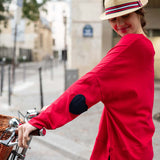 Woman in a red shirt and straw hat with a striped band, standing next to a bicycle on a city street.