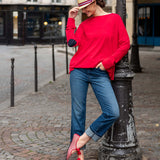 Woman in red sweater and blue jeans leaning against a lamp post on a street.