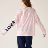 Person wearing a pink sweatshirt with 'LOVE' on the sleeve against a plain background