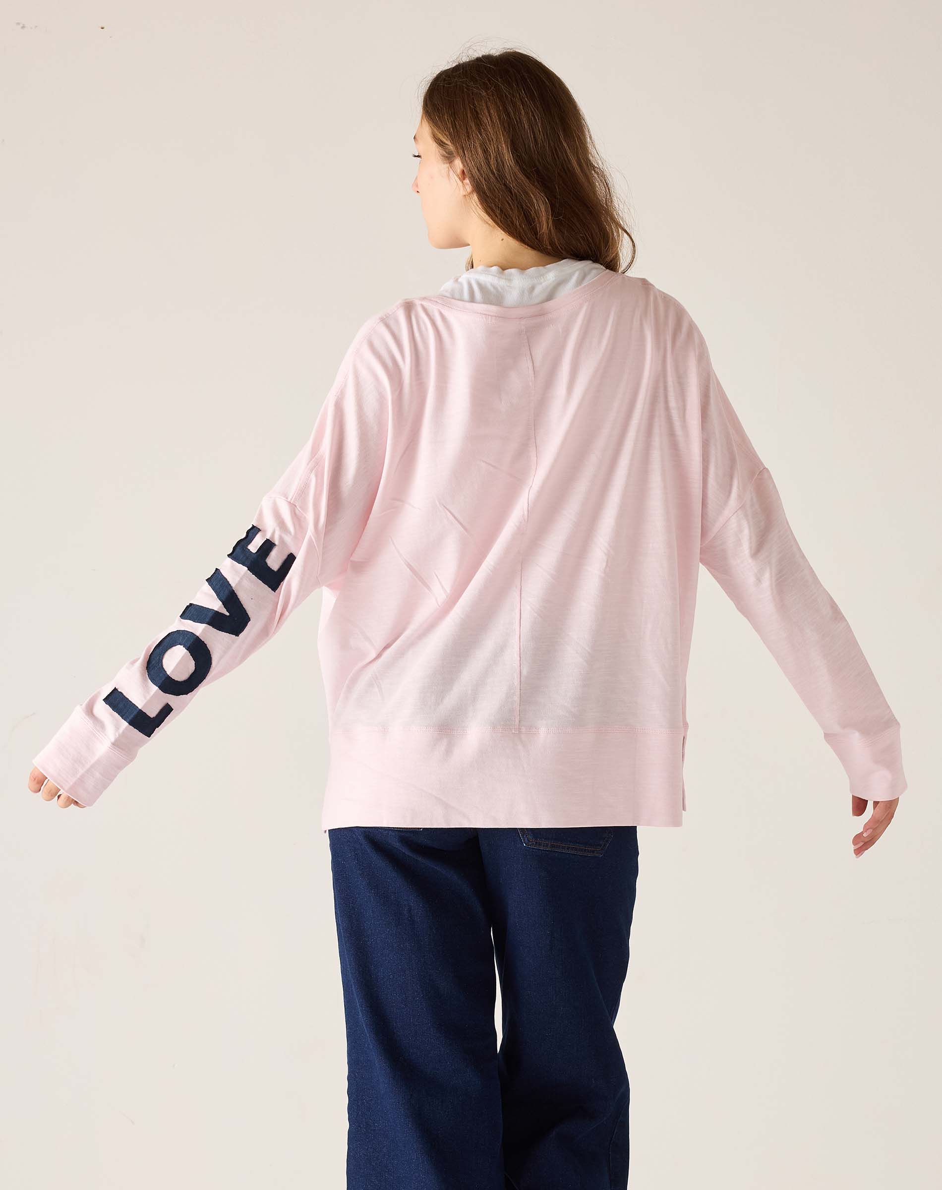 Person wearing a pink sweatshirt with 'LOVE' on the sleeve against a plain background
