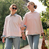 Two women walking outdoors, both wearing light pink sweaters and jeans.