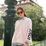 Woman in a pink sweatshirt with 'LOVE' on it standing in front of the Eiffel Tower.