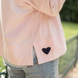 Light pink jacket with a black heart patch worn outdoors