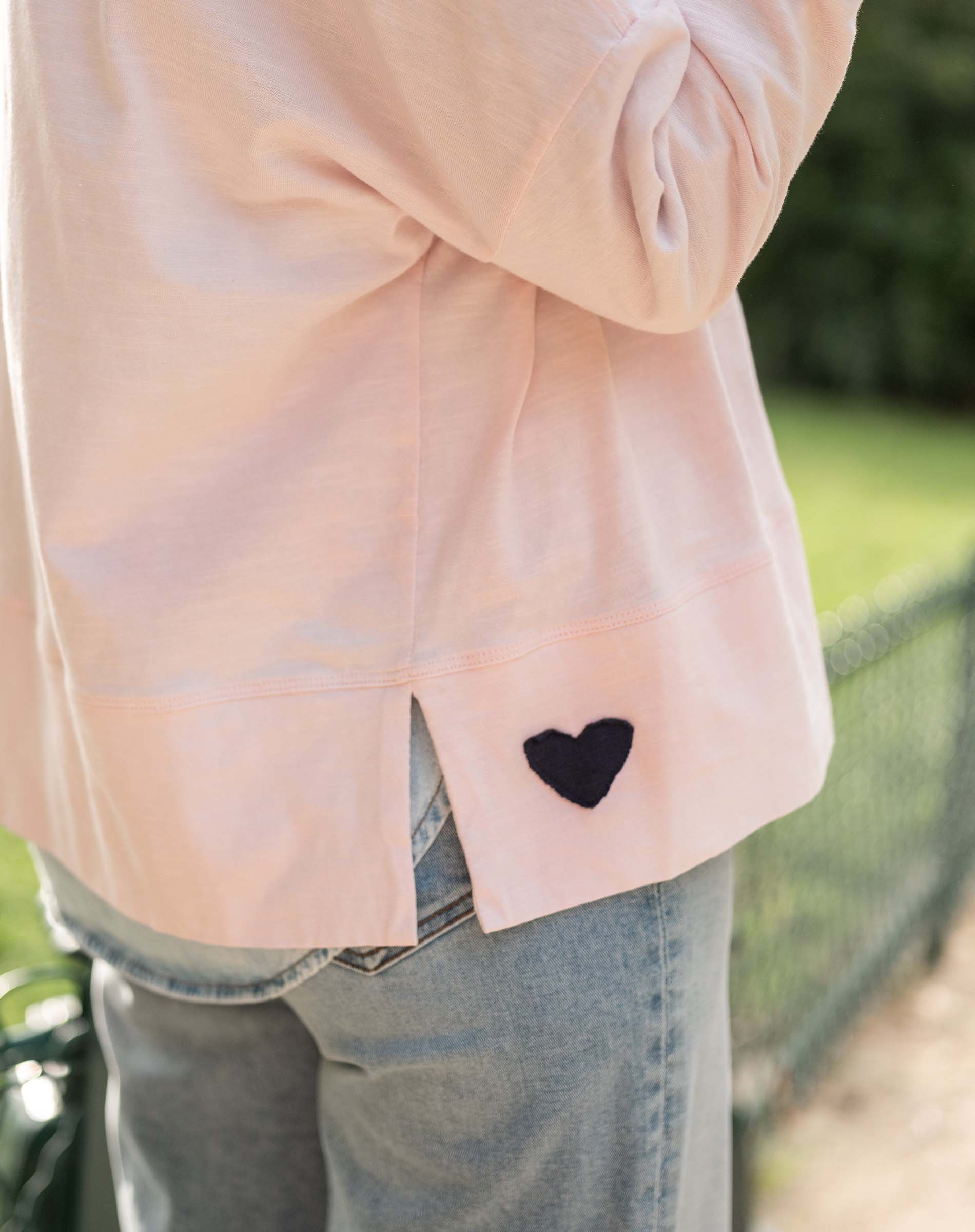 Light pink jacket with a black heart patch worn outdoors