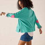 Woman wearing a teal sweater with pink elbow patches on a beige background