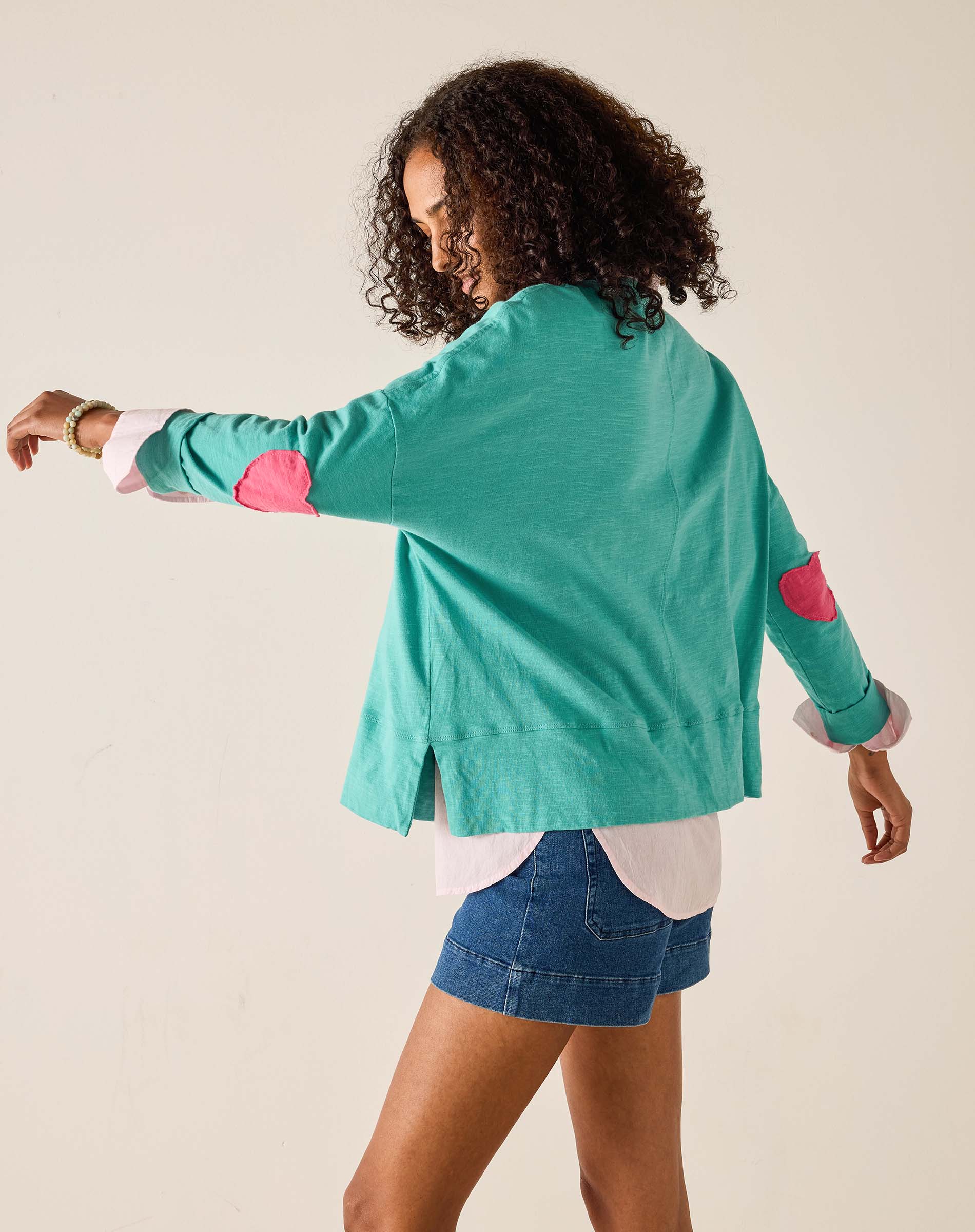 Woman wearing a teal sweater with pink elbow patches on a beige background