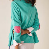 Person wearing a teal sweater with pink heart designs on a plain background