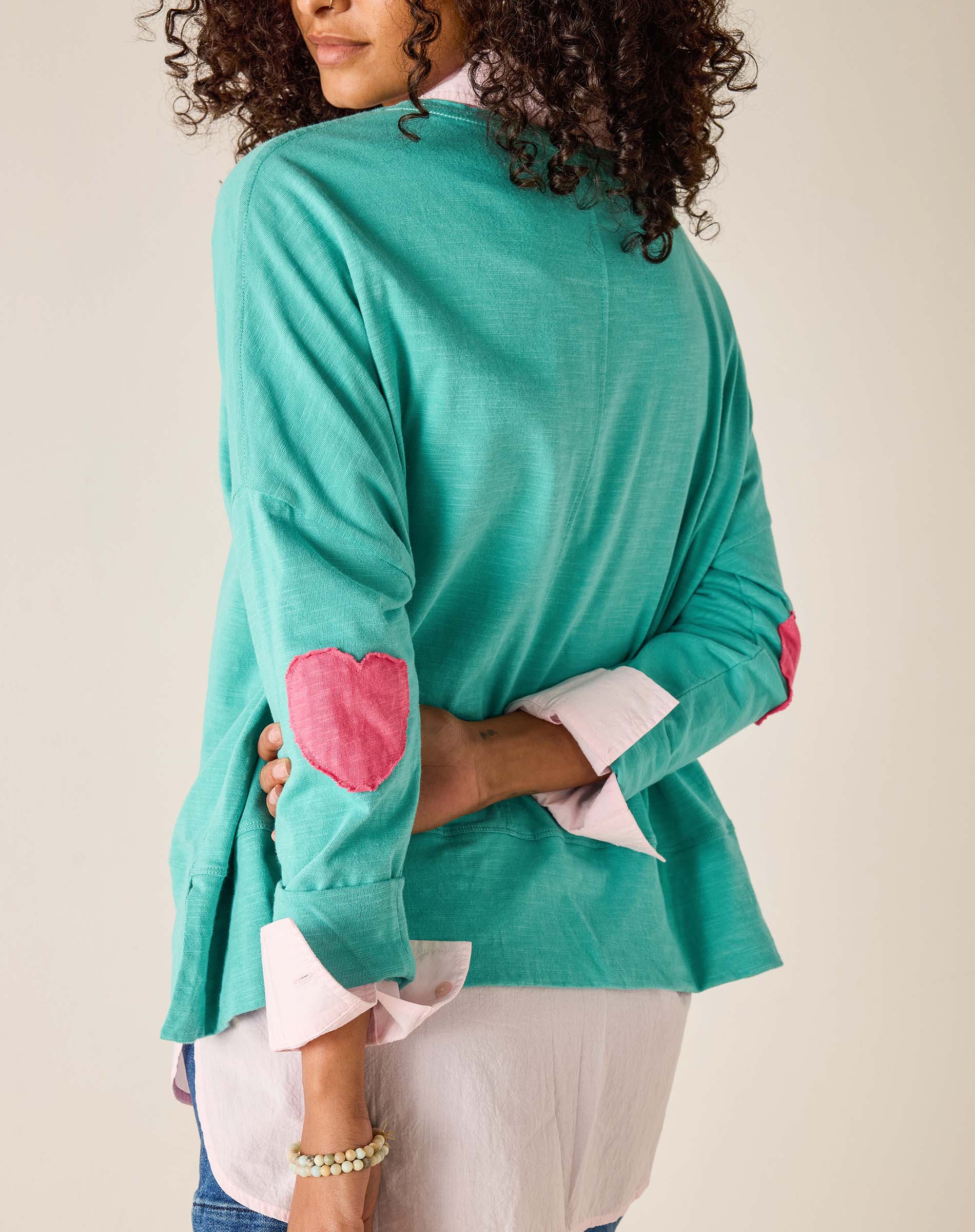 Person wearing a teal sweater with pink heart designs on a plain background
