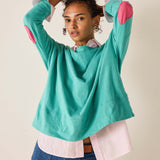 Person wearing a teal sweater with pink elbow patches on a beige background