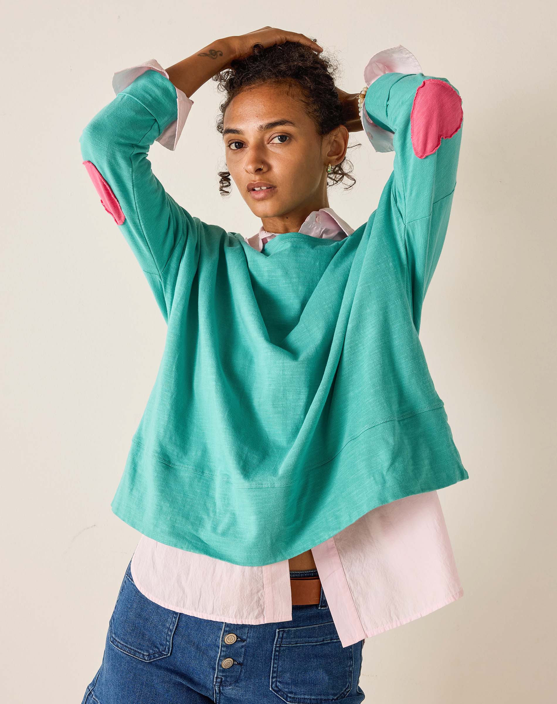 Person wearing a teal sweater with pink elbow patches on a beige background