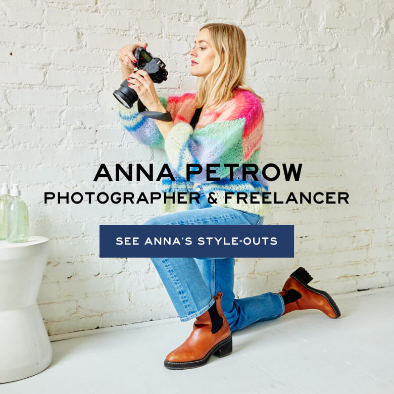 Anna Petrow in Blue Jeans and Multi-Colored Pastel Sweater on one Knee Holding Camera over a Table with Hand Soaps