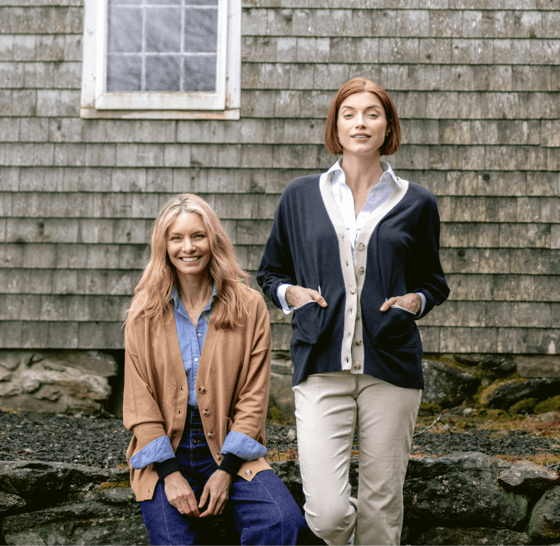 Two female wearing a camel and navy cardigan in front of stone wall