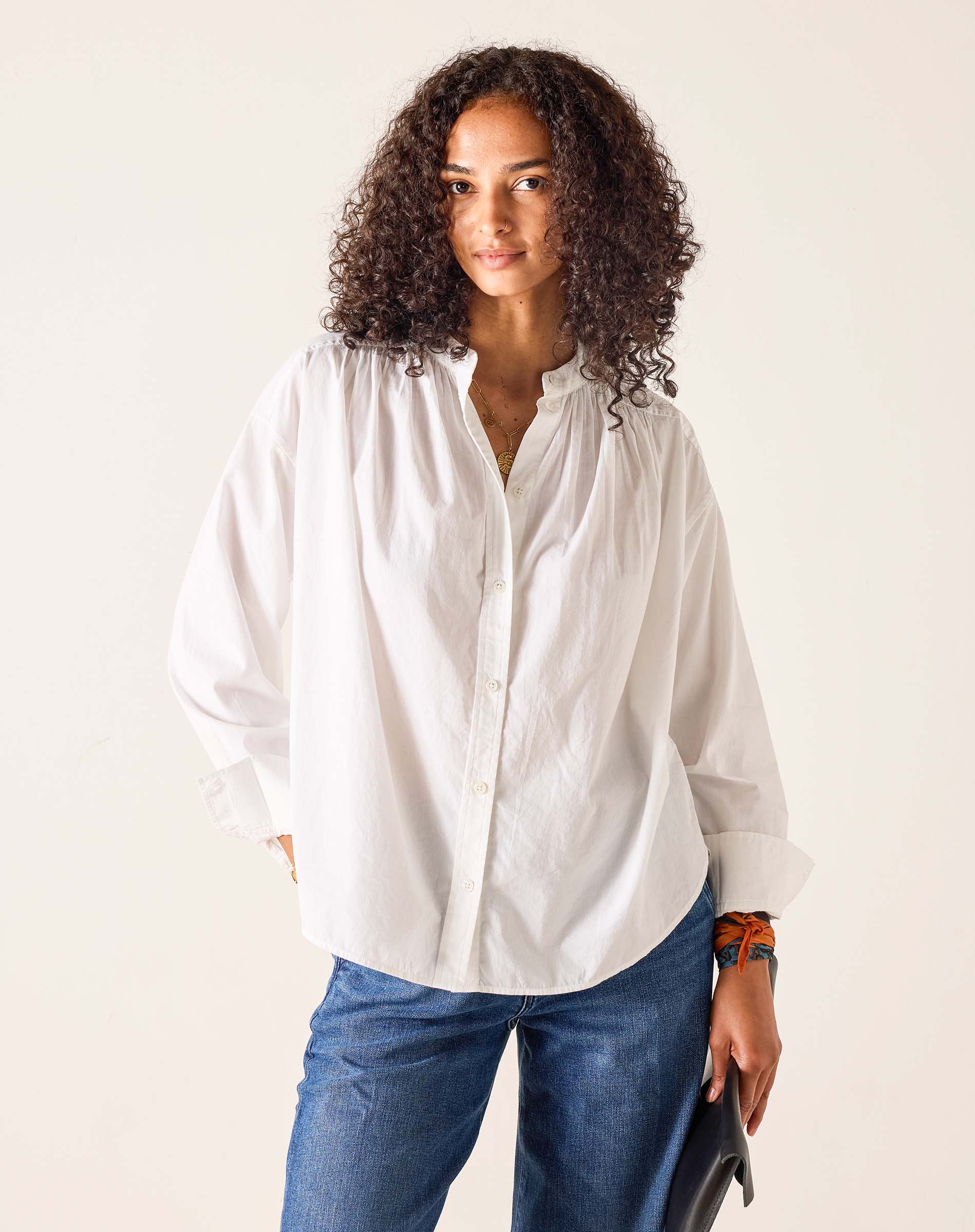 Woman wearing a white shirt and blue jeans against a plain background