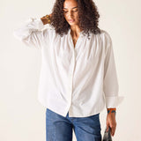 Woman wearing a white blouse and blue jeans against a plain background