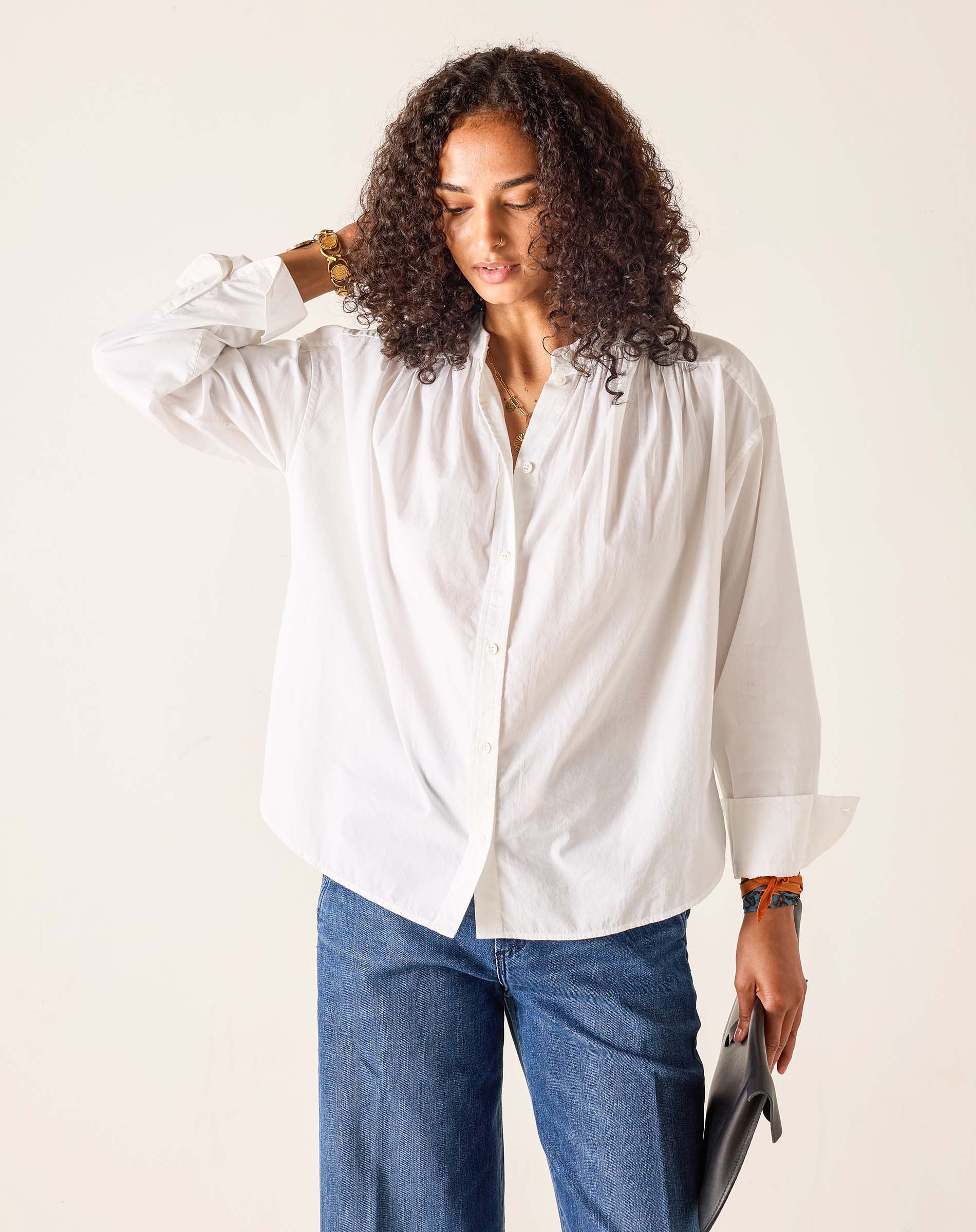 Woman wearing a white blouse and blue jeans against a plain background