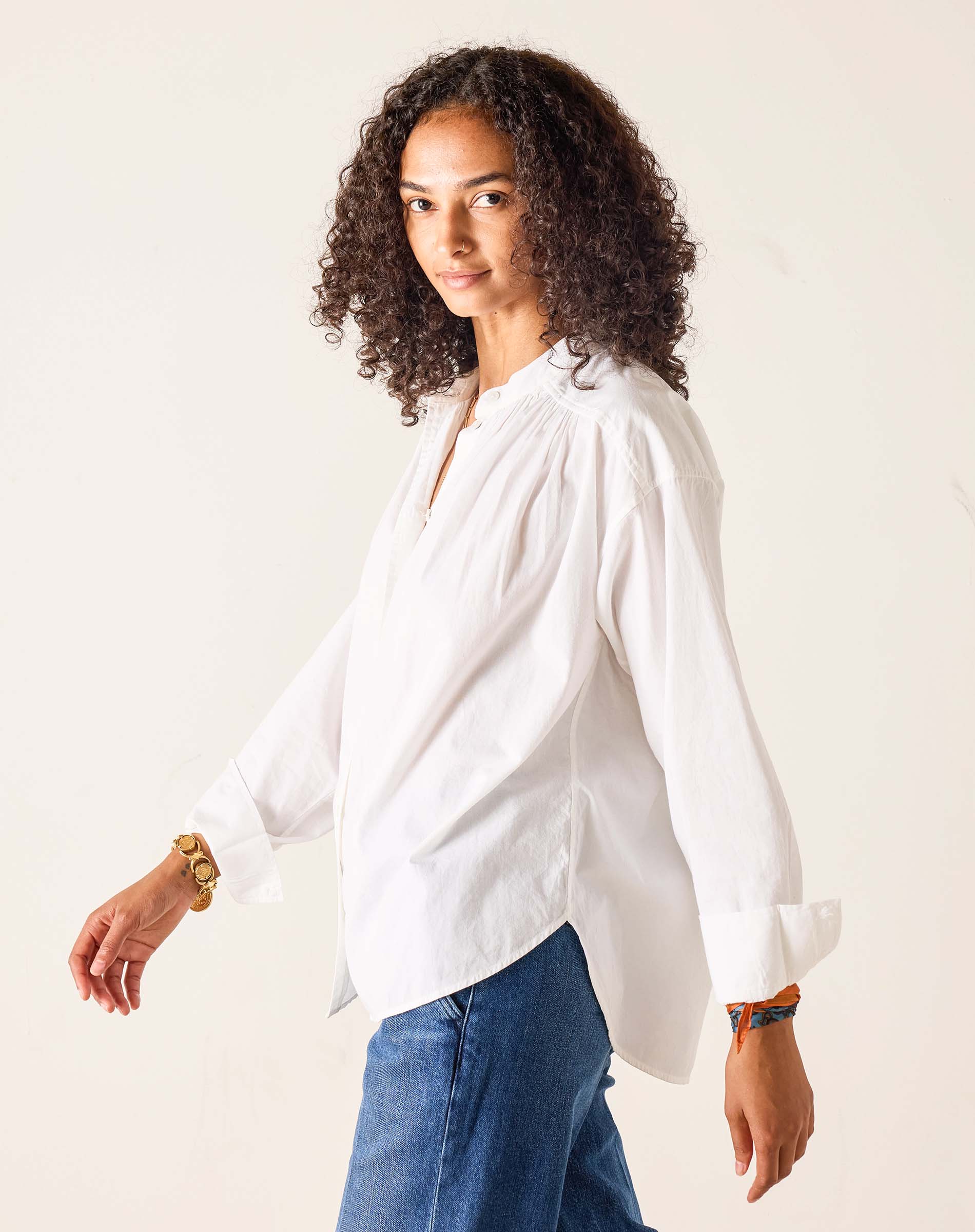 Woman wearing a white blouse and blue jeans against a plain background
