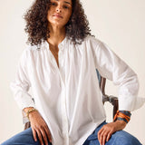 Woman wearing a white shirt and blue jeans sitting on a chair against a plain background
