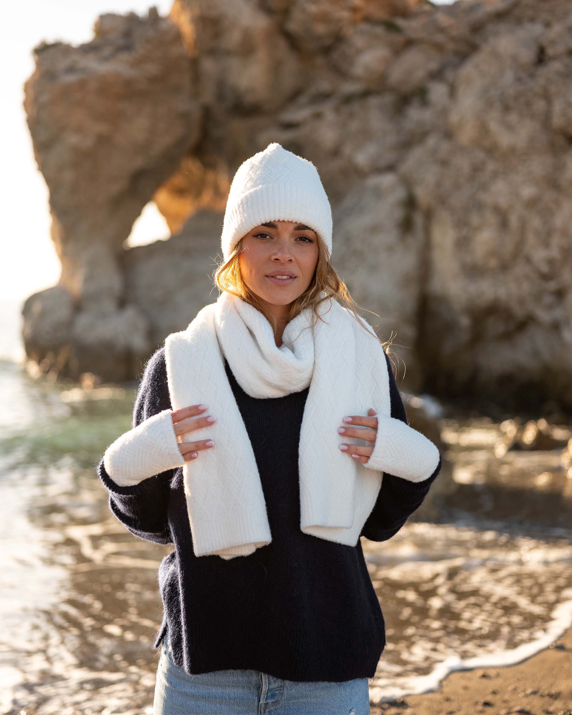 woman wearing mersea whisper white apres scarf beanie and fingerless gloves standing on beach