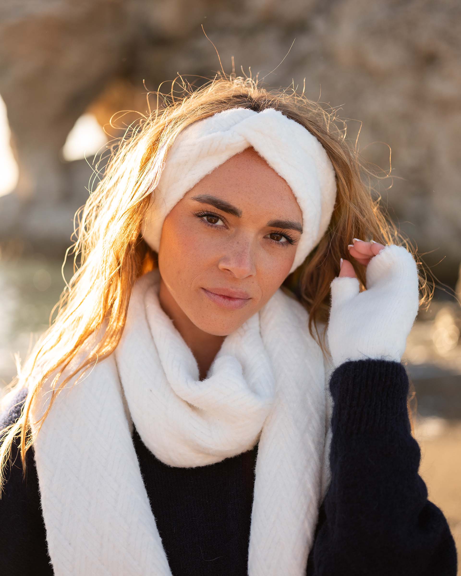 closeup of woman wearing mersea whisper white apres scarf headband and fingerless gloves standing on beach