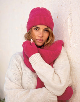 woman wearing mersea rasberry apres beanie and scarf standing against wall