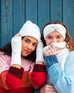closeup of two women wearing mersea whisper white apres headband fingerless gloves and beanie standing against blue door