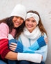 closeup of two women wearing mersea whisper white apres headband fingerless gloves and beanie against wall