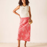 Woman wearing a white sleeveless top and pink patterned skirt against a white background