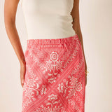 Person wearing a white top and red patterned skirt on a plain background