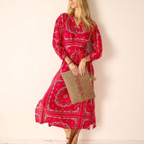 Woman wearing a red patterned dress holding a woven bag against a beige background