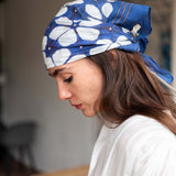 Woman wearing a blue headscarf with white patterns, looking downwards.