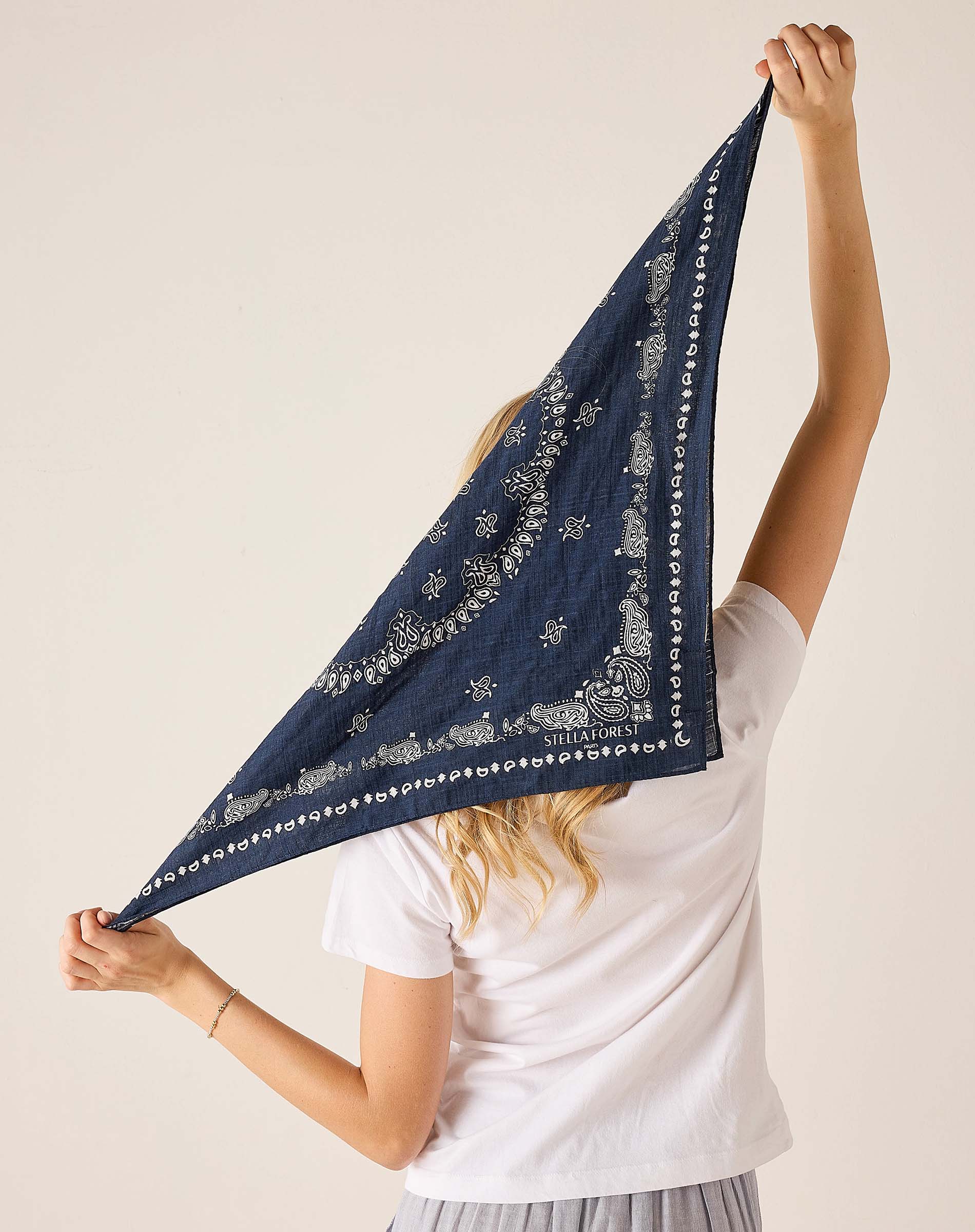 Person holding a navy blue bandana with white patterns against a plain background