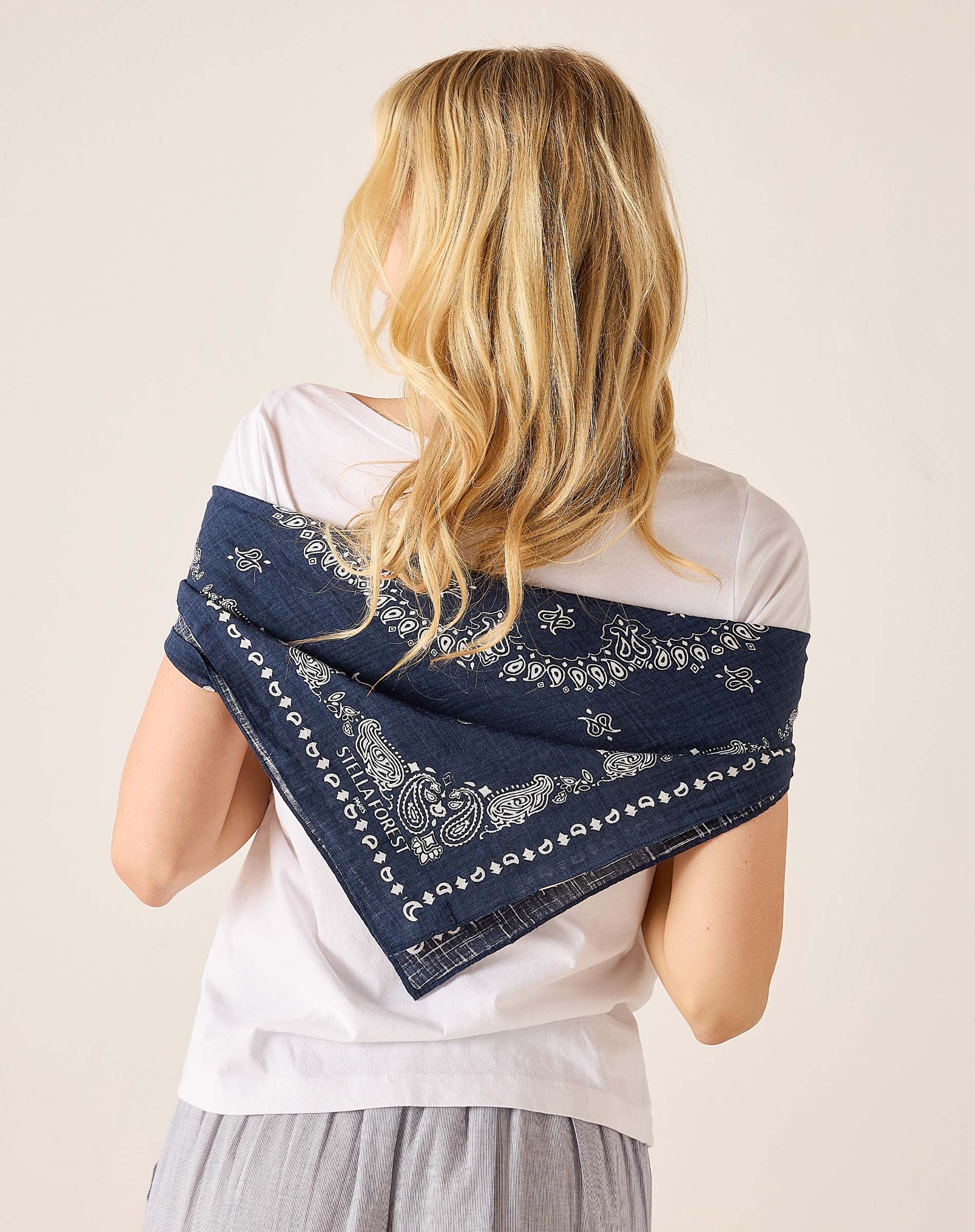 Woman wearing a navy blue bandana with white patterns over her shoulder on a beige background