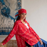 Woman wearing a red patterned jacket and headscarf sitting on a wicker chair.