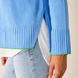 Light blue sweater with green trim worn over a white shirt and light jeans.
