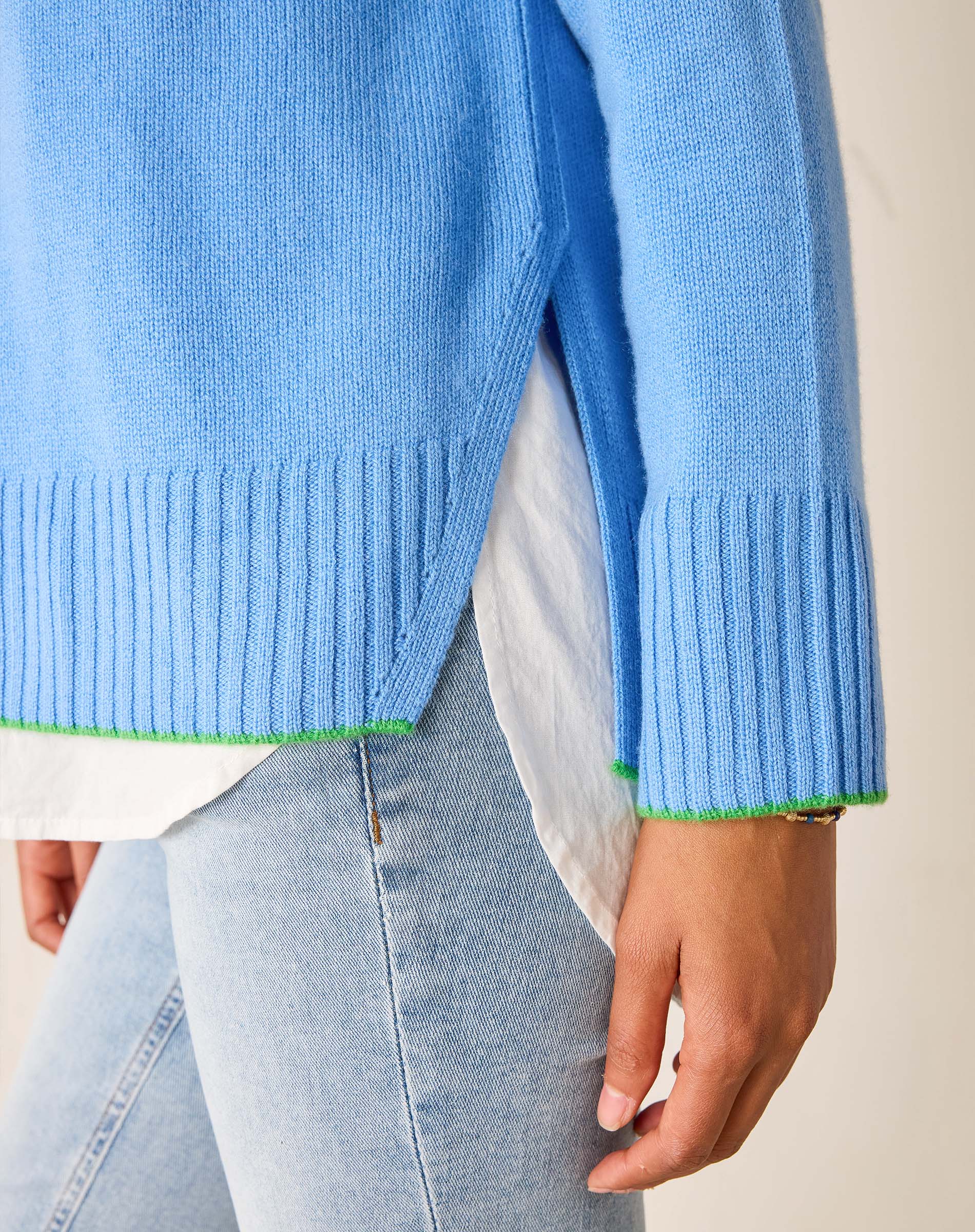 Light blue sweater with green trim worn over a white shirt and light jeans.