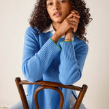 Woman wearing a blue sweater sitting on a wooden chair against a plain background