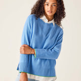 Woman wearing a blue sweater over a white shirt on a plain background