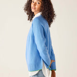 Woman wearing a light blue sweater with a white shirt underneath on a beige background