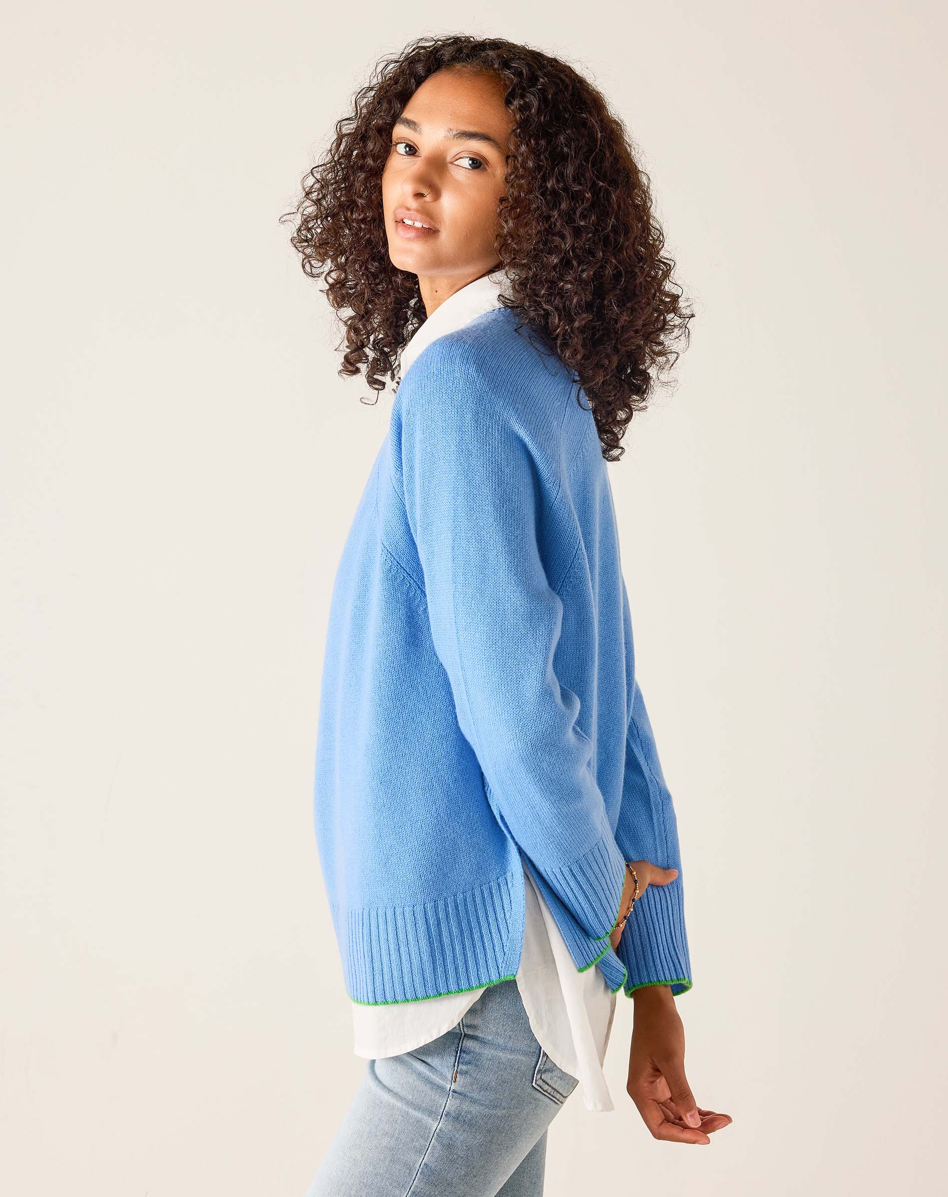Woman wearing a light blue sweater with a white shirt underneath on a beige background