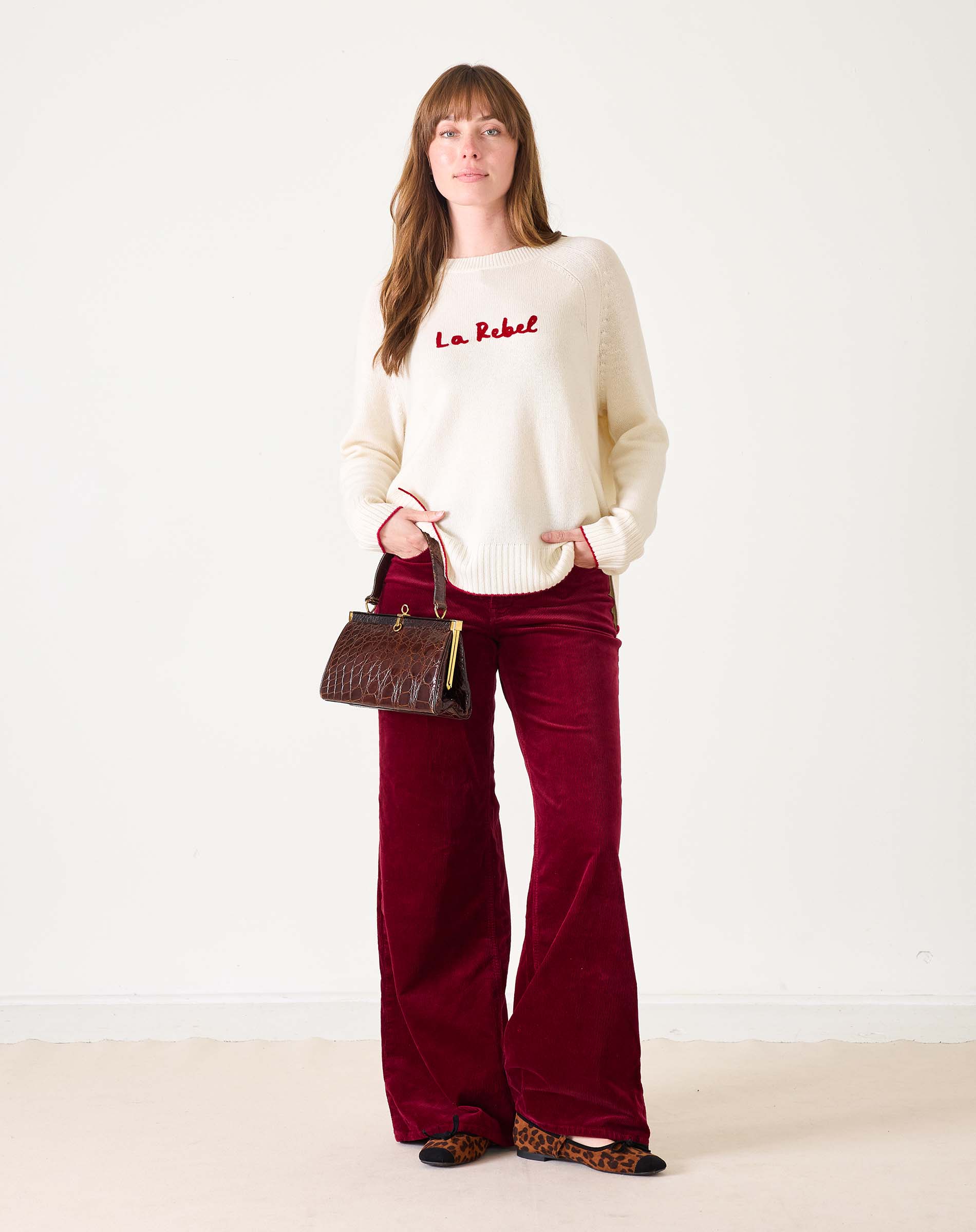 White sweater with red text 'La Rebel' worn by a person on a white background