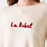 White sweater with red text 'La Rebel' worn by a person on a white background