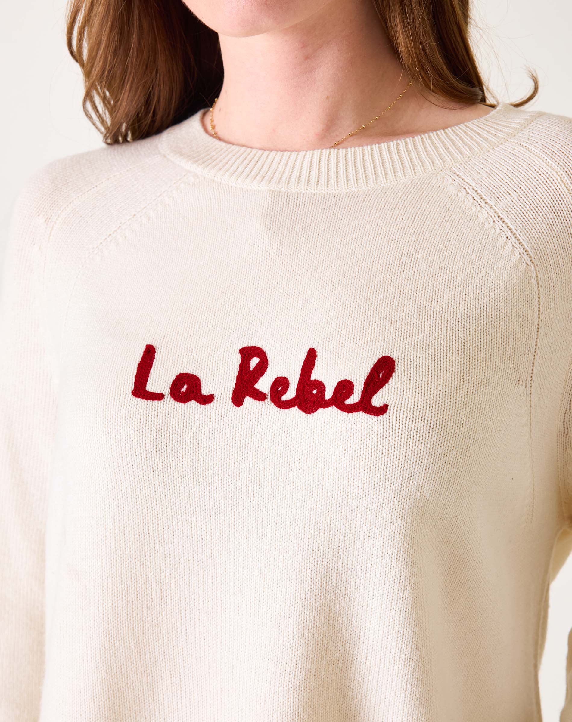 White sweater with red text 'La Rebel' worn by a person on a white background