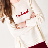 White sweater with red text 'La Rebel' worn by a person on a white background