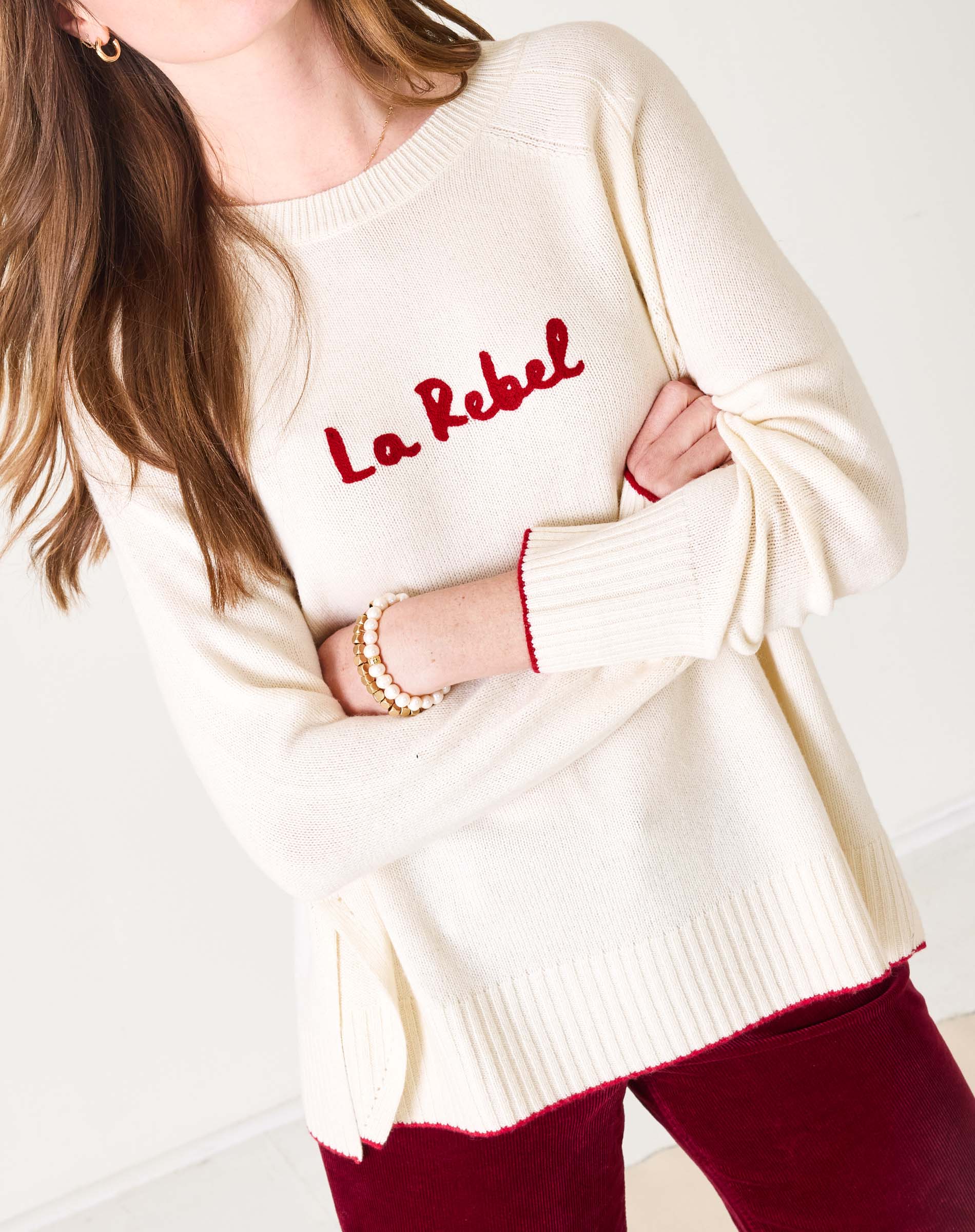 White sweater with red text 'La Rebel' worn by a person on a white background